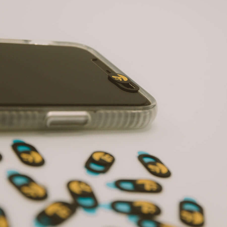 Phone with a cam cover on a white surface with small cam covers scattered around
