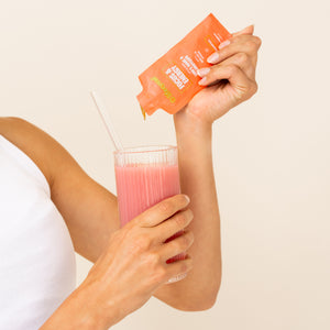 Arm holding glass of pink liquid with glass straw and Lifecykel liposomal packet pouring to the glass