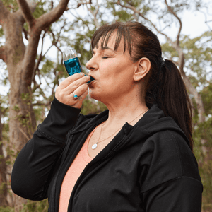 Woman wearing black jacket using the Air Physio blue breathing device
