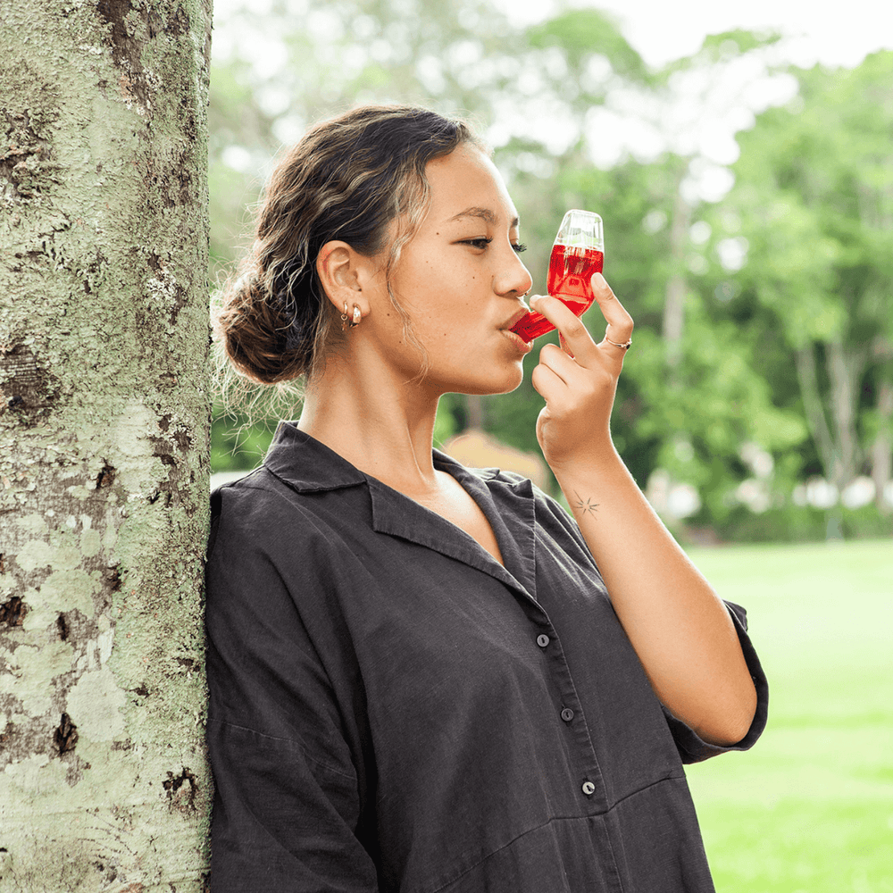 Woman wearing dark top sleeve leaning on the tree using the red breathing device