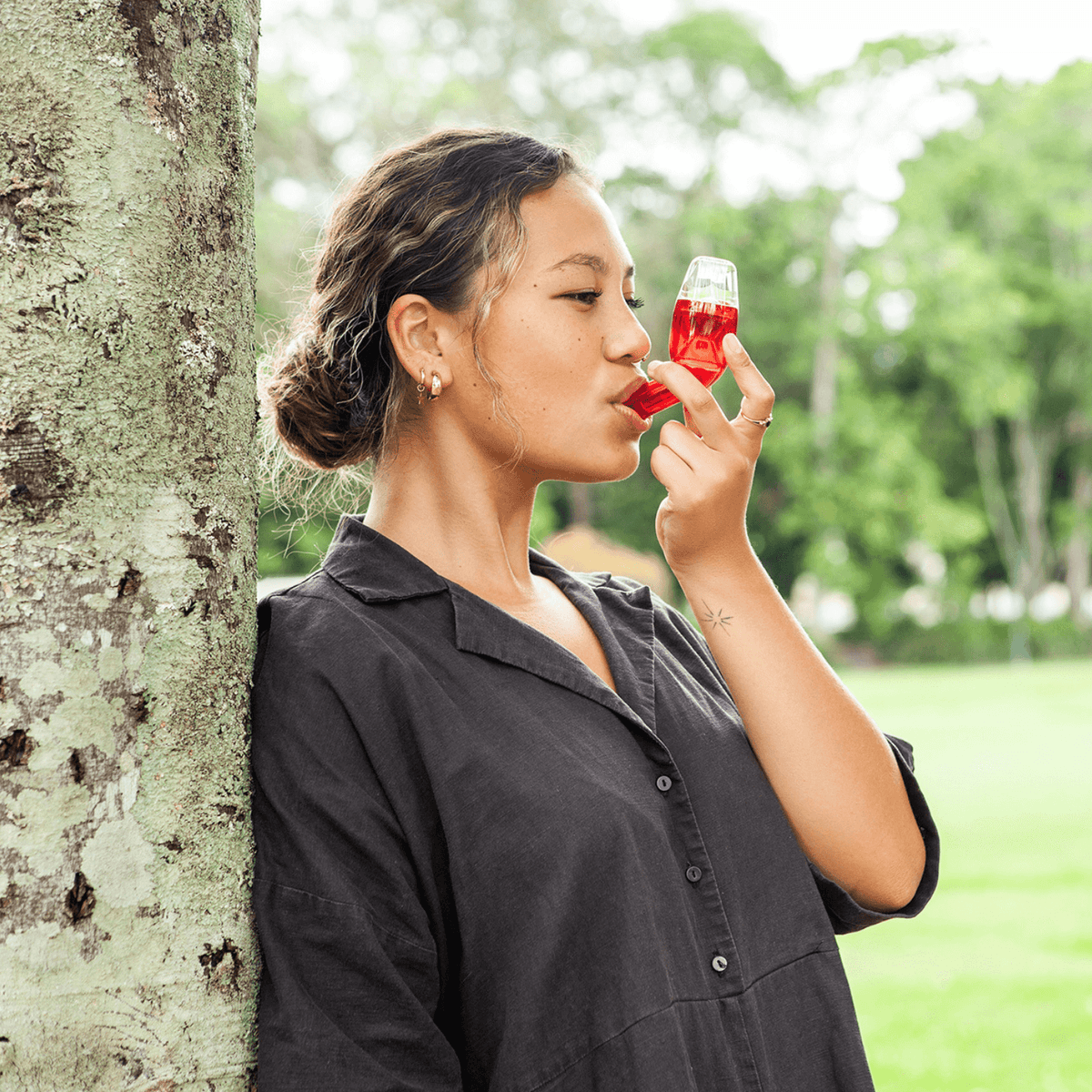 Woman wearing dark top sleeve leaning on the tree using the red breathing device