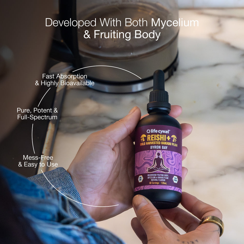 Hand holding a bottle of Lifecykel Reishi mushroom extract supplement with text highlighting features, against a blurred kitchen background.