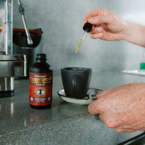 A Lifecykel Cordyceps mushroom extracts supplements with a hand with dropper pouring liquid to black ceramic mug 